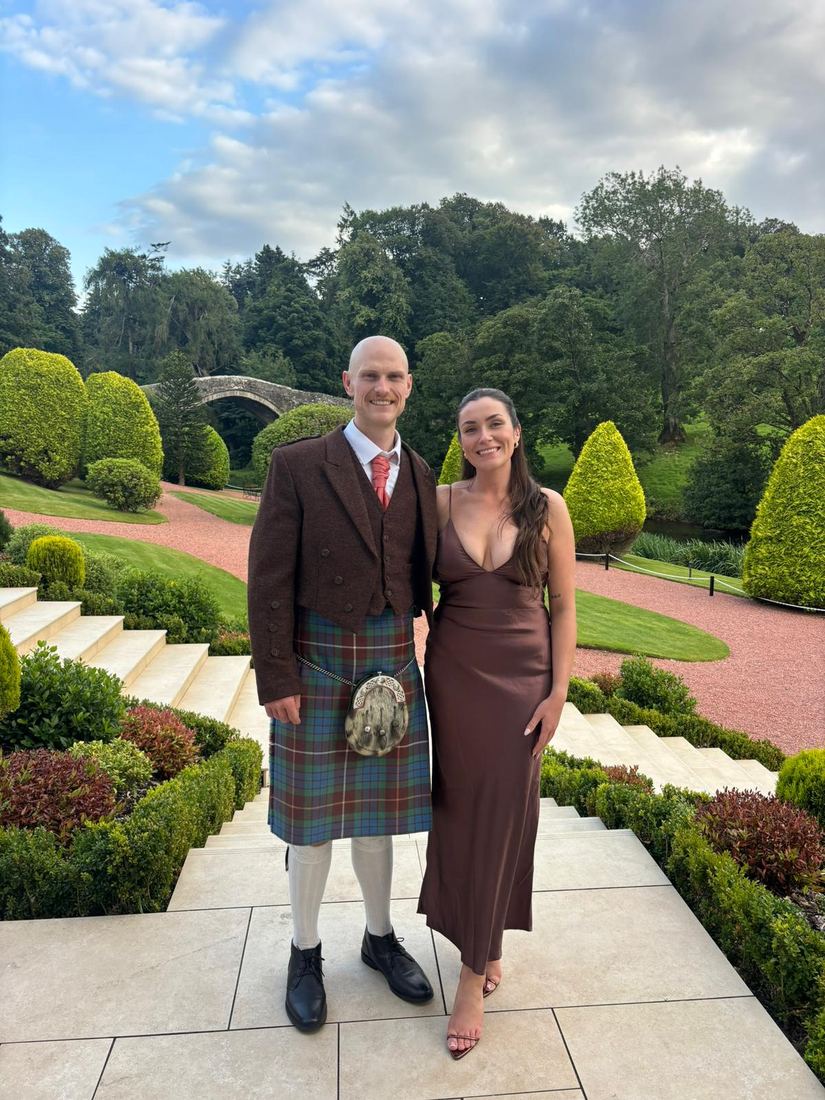 Reece in a kilt and Robyn in a brown silk dress in manicured gardens